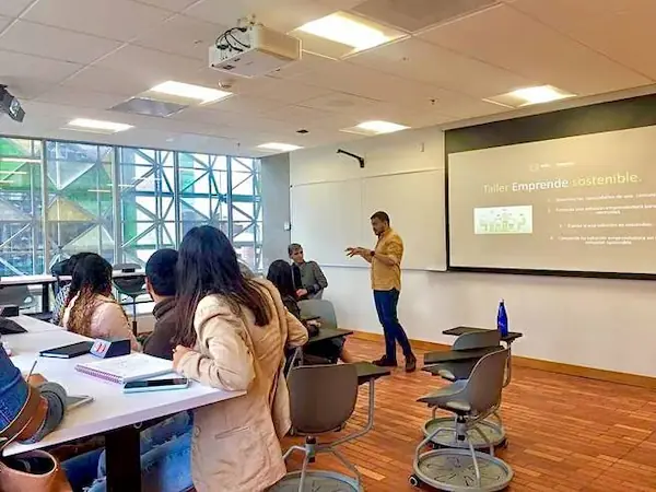 Docente liderando un taller educativo en un aula moderna con estudiantes comprometidos